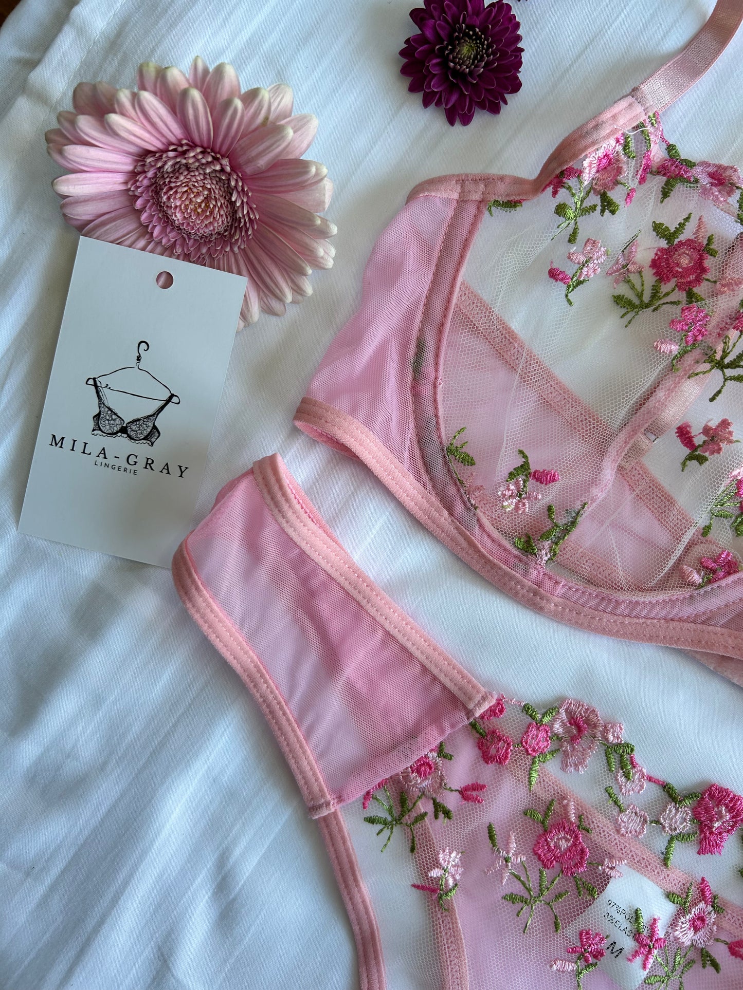 A delicate pink lingerie set with peony floral embroidery, displayed alongside a matching hair accessory and with a brand tag visible.