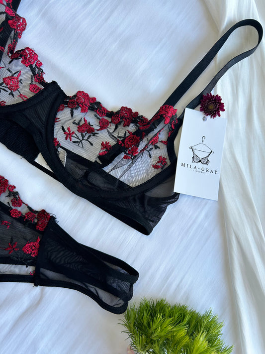 A black lace underwire bra with red rose embroidery, displayed on a white background with a tag showing the brand name.