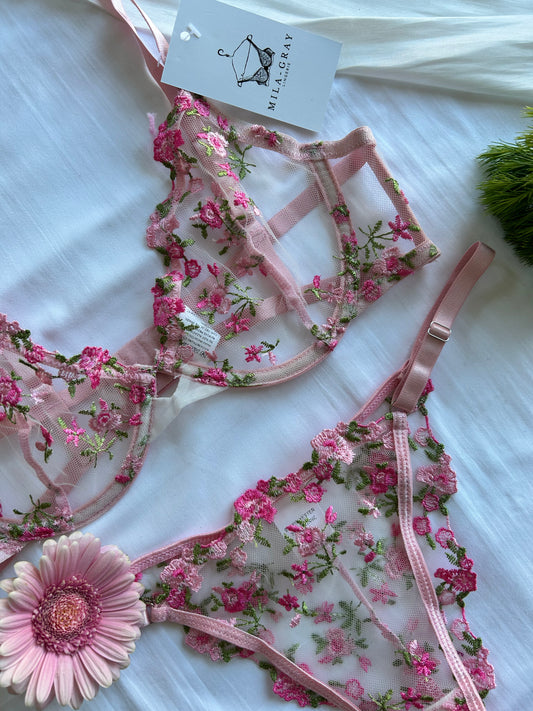 A lingerie set with floral embroidery, featuring pink straps and a underwire bra, laid out on a white surface with a tag attached.